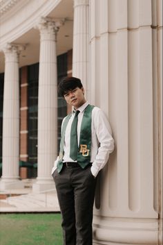 a young man leaning against the side of a building wearing a green vest and tie