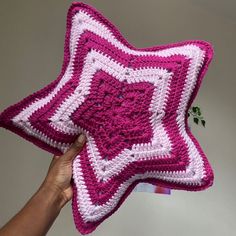 a hand holding a pink and white crocheted star pillow