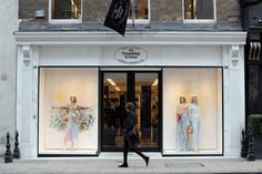 a woman walking past a store front with mannequins in the window display