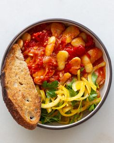 a bowl filled with pasta and vegetables next to a piece of bread