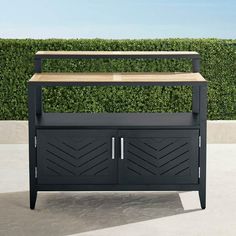 a black outdoor bar with wooden top and doors on the outside, in front of a hedge