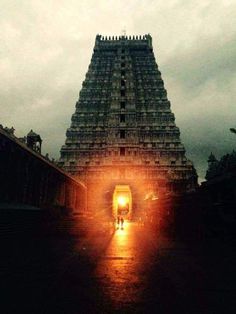 a very tall building with some lights on it's sides and people walking in the doorway