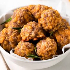 a white bowl filled with meatballs covered in sauce and garnished with rosemary