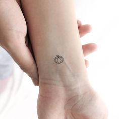 a small tattoo on the wrist of a woman's left arm, with an apple