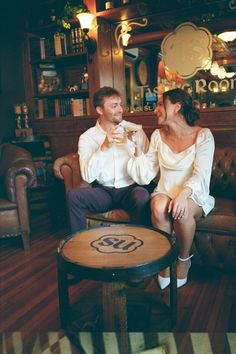 a man and woman sitting on a couch in a room with wooden floors, smiling at each other