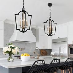 a kitchen with white cabinets and marble counter tops, two chandeliers hanging from the ceiling