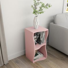 a pink shelf with a vase and books on it in front of a white couch