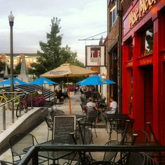 people sitting at tables outside an outdoor restaurant with umbrellas on the side walk way