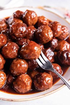 a white plate topped with meatballs covered in gravy next to a fork