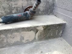 a drill that is laying on some concrete steps next to a cement wall with a pipe sticking out of it