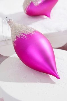 two shiny pink christmas ornaments sitting on top of white plates