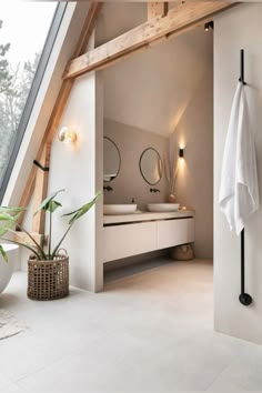 a white bathroom with two sinks and a large window in the corner, along with a potted plant