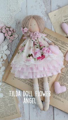 a doll is laying on top of an open book with flowers and hearts around it