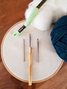 yarn, needles and knitting needles on a wooden table with a ball of yarn next to it