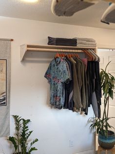 clothes are hanging on a rack in the corner of a room next to a potted plant