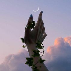 a woman's hand with nail polish holding up a crescent moon above the clouds