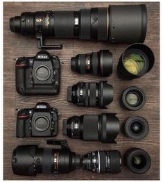 many different cameras sitting on top of a wooden table next to lenses and camera accessories