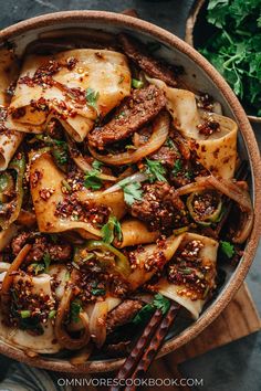 a bowl filled with meat and vegetables on top of a wooden cutting board next to some chopsticks