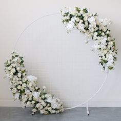 white flowers are arranged in the shape of a crescent on a circular metal stand against a wall