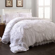 a white comforter with ruffles on it and two framed pictures above the bed