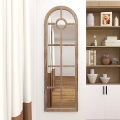 an arched mirror is hanging on the wall next to bookshelves and vases