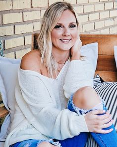 a woman sitting on top of a bed next to a brick wall and smiling at the camera