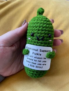 a hand holding a small green crocheted stuffed animal with a tag on it