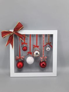 an ornament in a white frame decorated with red and silver balls, bows and ribbons