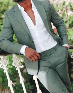 a man in a green suit and white shirt is leaning on a railing with his hand on his hip