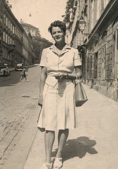 an old black and white photo of a woman walking down the street