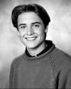 a black and white photo of a young man in a sweater smiling at the camera