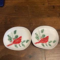 two plates with red birds and holly on them sitting on a wooden floor next to each other