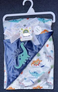 a blue and green dinosaur blanket hanging on a hanger with its tag attached to it