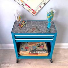 a blue table with magazines on it in front of a game board and wall hanging