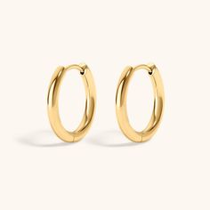 the gold hoop earrings are small and shiny, with an oval design on each side