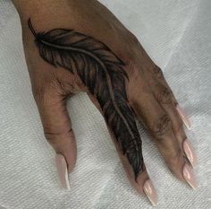 a woman's hand with a black feather tattoo on it