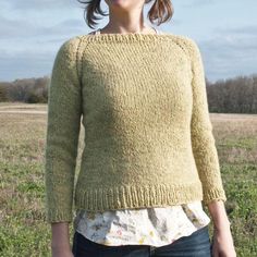 a woman standing in a field wearing a yellow sweater