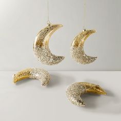 three pieces of gold and silver glittered moon ornaments hanging from strings on a white surface