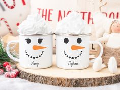 two snowman mugs sitting on top of a wooden table next to christmas decorations