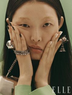 a woman with long black hair holding her hands to her face and wearing rings on her fingers