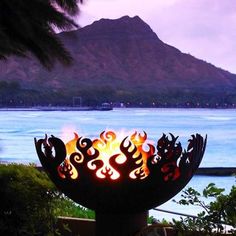 a fire pit sitting on top of a lush green field next to the ocean with mountains in the background