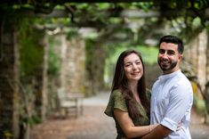 a man and woman posing for a photo in the park under an arbor with trees