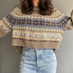 a woman wearing a sweater and jeans with her hands in the air while standing against a wall