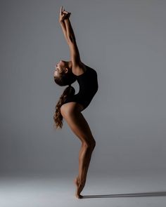 a woman in a black leotard doing a dance pose with her arms up