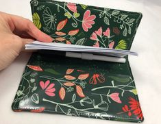 a hand holding an open wallet on top of a white table with red and green flowers