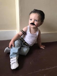 a little boy sitting on the floor with a fake moustache on his face