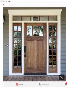 a wooden door on the side of a gray house with two glass panes above it