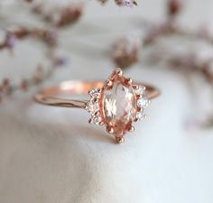 a close up of a ring with an oval shaped peach colored stone surrounded by small white and pink flowers