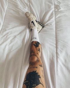 a person's foot with tattoos on it laying on a white bed sheet in front of a pillow