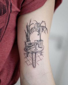 a woman's arm with a tattoo on it that has a table and potted plant